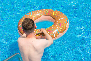 young man with rubber ring in suumer swimming pool  - 605817028