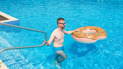 young man with rubber ring in suumer swimming pool  - 605817042
