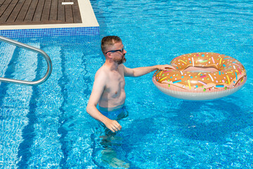 young man with rubber ring in suumer swimming pool  - 605817052