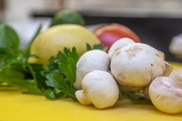 Kitchen composition of fresh vegetables and herbs. Appetizing tomato, cucumber, garlic, raw champignons lie on a light textured table