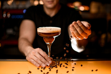 Barman sprinkles with coffee beans glass with martini espresso cocktail at bar counter
