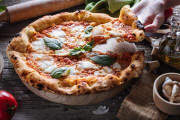 Pizza Napoletana, traditional and authentic Italian pizza baked in wood fired oven. Margherita pizza with mozzarella cheese, tomato sauce, olive oil and basil leaves. On wooden board with ingredients.