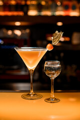Bar counter with two alcoholic drinks: glass with sparkling wine and fresh martini cocktail decorated with physalis