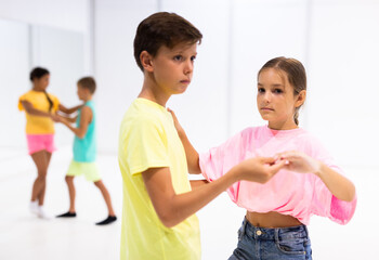 Positive preteen children learning to dance waltz in pairs in choreography class.