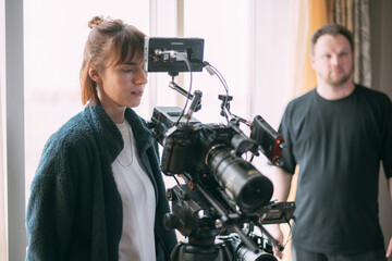 The director of photography is a woman behind a video camera on the set.  A professional videographer at work on the filming of a movie