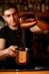 Handsome male bartender pouring fuming alcoholic drink from one steel cup to another