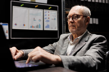Accountant employee checking administrative analytical statistics in dark cabinet room office. Professional businessman in file storage room surrounded by accountancy reports