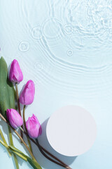 Podium or pedestal with water ripple and tulips flat lay, top view. Cosmetic template, copy space