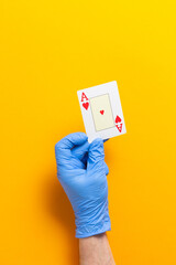 Hand with blue surgical glove holding an ace of hearts card on orange background.