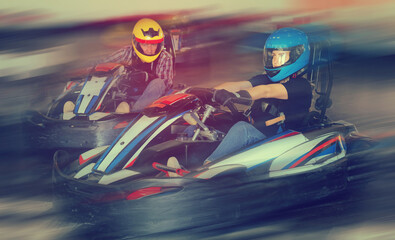 Group of nice male and females in helmets driving racing cars at kart track.