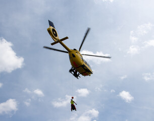 Yellow search and rescue helicopter lifting someone off the ground