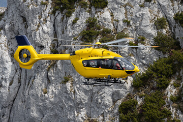 Close-up shot of a yellow search and rescue helicopter with a rocky cliff in the background
