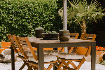 Outdoor garden furniture. Wooden table, chairs in the backyard. Decorative flower pots standing on table. Terrace yard in daytime. Lounge place to relax outdoors in sunny day. Brown wood table chairs