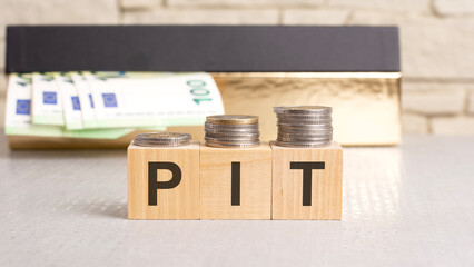 wooden blocks with letters PIT - acronym from Personal Income Tax, a box of euro bills in the background
