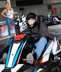 Diligent efficient man in helmet driving car for karting in sport club, friendly smiling woman with...