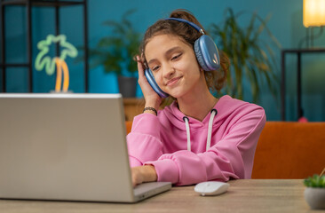 Caucasian preteen school girl in headphones use laptop listens to music or lesson, distance...