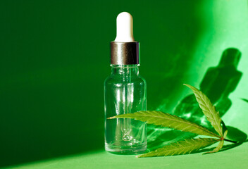 A glass bottle pipette and cannabis leaf on green background with copy space. CBD hemp oil, THC...