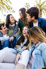 Vertical photo of happy group of millennial friends having fun sitting outdoors. Diverse college...