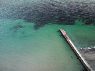 Aerial top down view of old concrete pier or breakwater with emerald sea water 