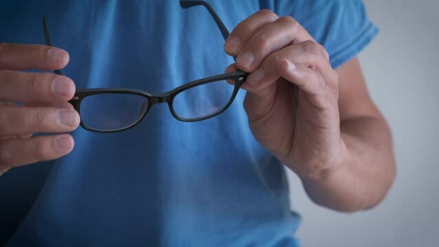 Male cleaning diopter glasses. A view of man cleaning his diopter glasses indoor. A concept of vision problems and trouble with glasses.