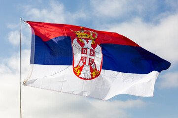 Flag of Serbia flutters in the wind against a blue sky background
