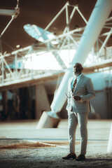 Vertical shot of a stylish bald business black man, with a long beard with white hair, dressed in a suit, holds a pair of sunglasses with a pensive expression in an architecturally beautiful space