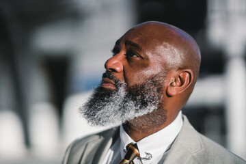 A close-up portrait of the profile of a charming black man with a long greying beard, dressed in a grey suit jacket, captured with selective focus, highlighting his distinguished features