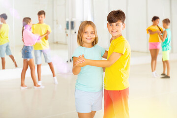 Interested modern tween boy and girl practicing slow pair dancing during group class in dance studio for children.