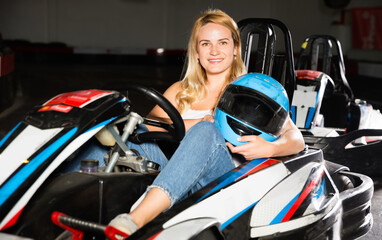 Young glad cheerful positive smiling woman with helmet sitting in car for karting in sport club