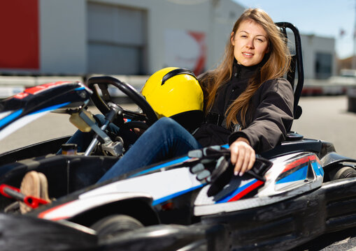 Portrait of glad female in helmet driving racing car at outdoors cart circuit