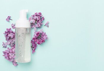 Foaming facial cleanser and with flowers on color background, top view