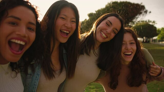Four happy girls laughing and hugging while standing on rain