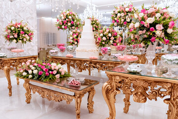 a golden wooden table, with a wedding cake in the center, decorated with vases of rose flowers and sweets