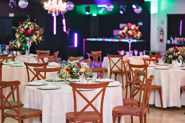a hall decorated with round tables with white tablecloths and wooden chairs