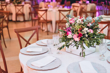 a glass dining table decorated with plates and flowers, with wooden chairs around it