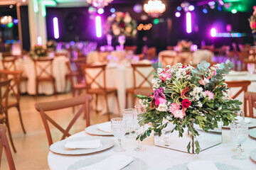 a glass dining table decorated with plates and flowers, with wooden chairs around it