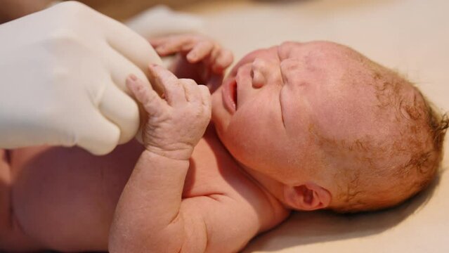 Newborn red-haired baby cries while doctor&rsquo;s gloved hand puts stethoscope to its chest. Checking the life of a child after birth. Close up.