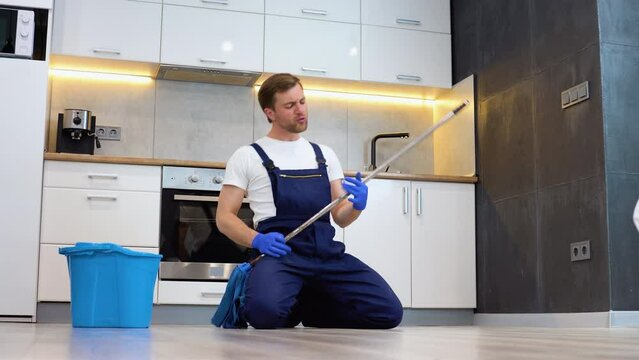Funny cheerful professional cleaner with mop depicts plays the guitar during a break. Rock star in the kitchen