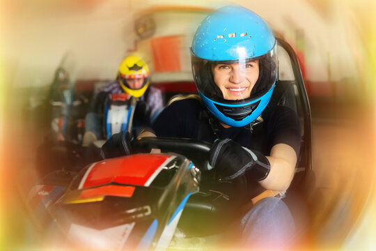Young woman in helmet and other people driving cars for racing in sport club indoor