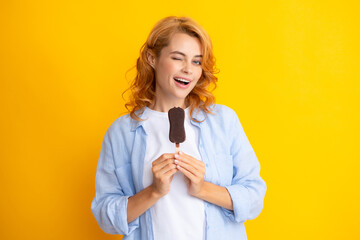 Summer concept. Winks woman holds tasty frozen ice cream, enjoys eating delicious cold dessert, poses on yellow background, feels happy.