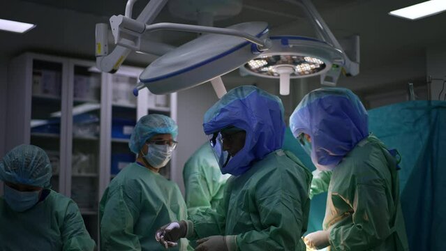 One surgeon of a big team turns to the nurse stretching hand for the instrument. Doctors in protective suits perform arthroscopic operation.