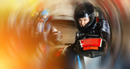Glad positive girl and her friends competing on racing cars at kart circuit - obrazy, fototapety, plakaty