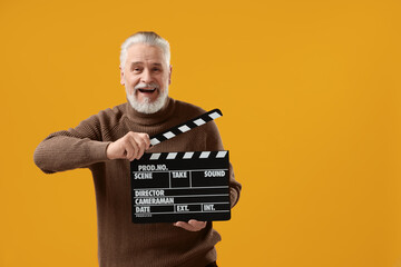 Senior actor holding clapperboard on yellow background, space for text. Film industry