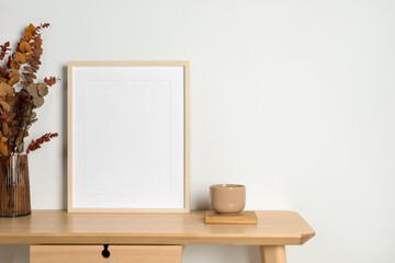 Empty photo frame, cup and vase with dry decorative leaves on wooden table. Mockup for design