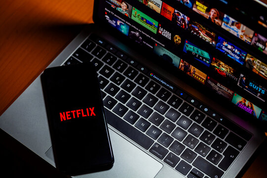 ITALY - May 24, 2023: Netflix homepage on a Mac laptop screen and lettering logo on the smartphone screen. Netflix is an online video streaming subscription service