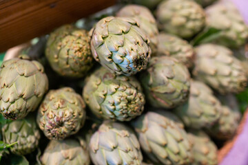 Fototapeta na wymiar Heap of raw ripe green artichokes offered for sale at farmers market stall. Healthy ecological nutrition concept