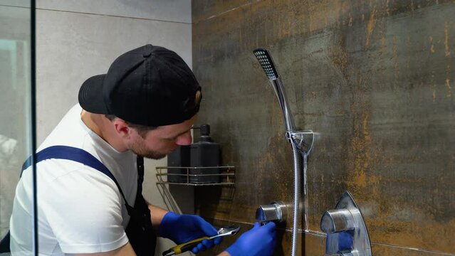 Young plumber man with tools repairing fixing faucet in shower stall