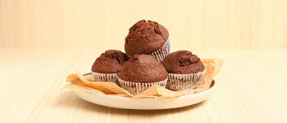 Plate with delicious chocolate muffins on light wooden background