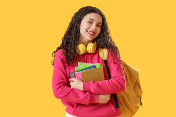 Female student with headphones, notebooks and backpack on yellow background