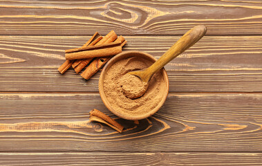 Bowl of cinnamon powder and sticks on wooden background